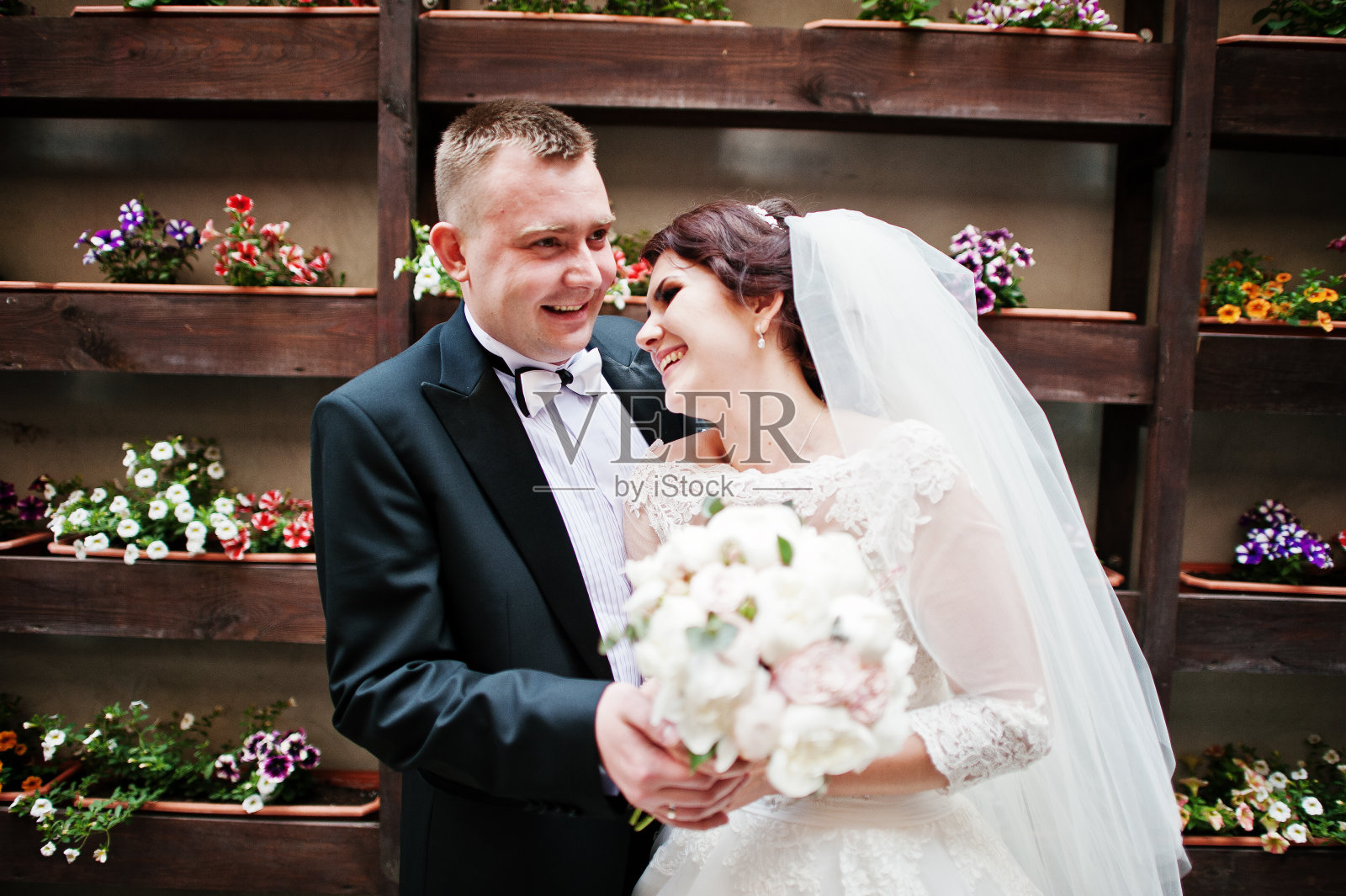 美丽的新婚夫妇留在背景墙与盆花。照片摄影图片