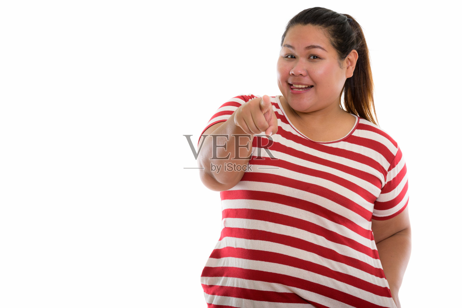 摄影棚拍摄的年轻快乐超重的亚洲妇女微笑着指着相机，并伸出舌头照片摄影图片