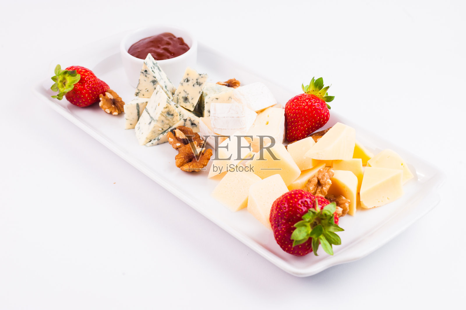 奶酪盘，配有奶酪，布里干酪，卡门贝尔奶酪和羊奶核桃，草莓和果酱，单独放在白色背景的盘子上照片摄影图片