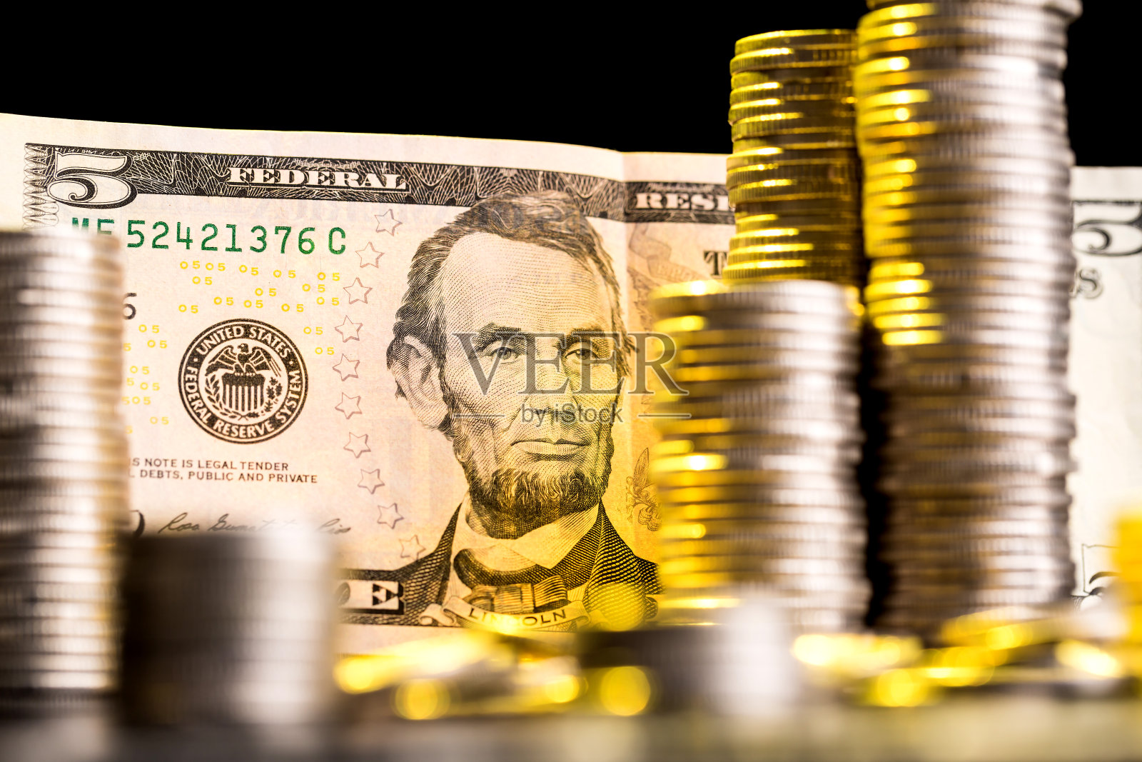 5美元钞票夹在一堆硬币中间。银行、现金兑换、购物和销售的概念。照片摄影图片