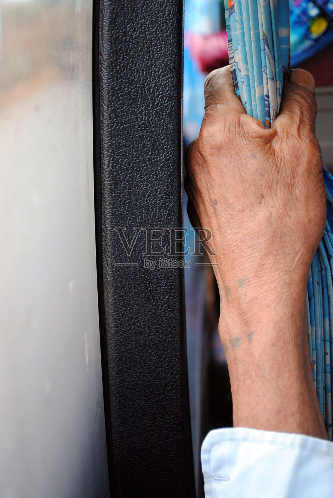 在公共汽车上，老人的手牵着蓝色的窗帘照片摄影图片