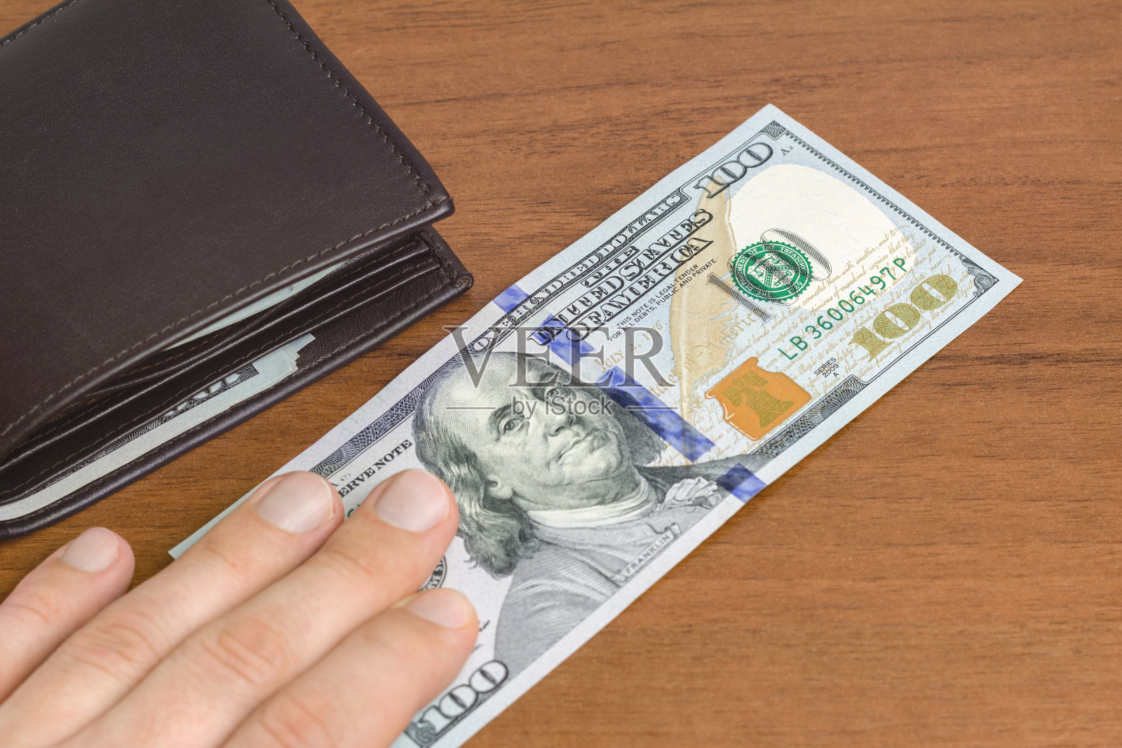 人已经把他的手放在百元钞票的木制背景上，特写，货币和金融的概念。照片摄影图片