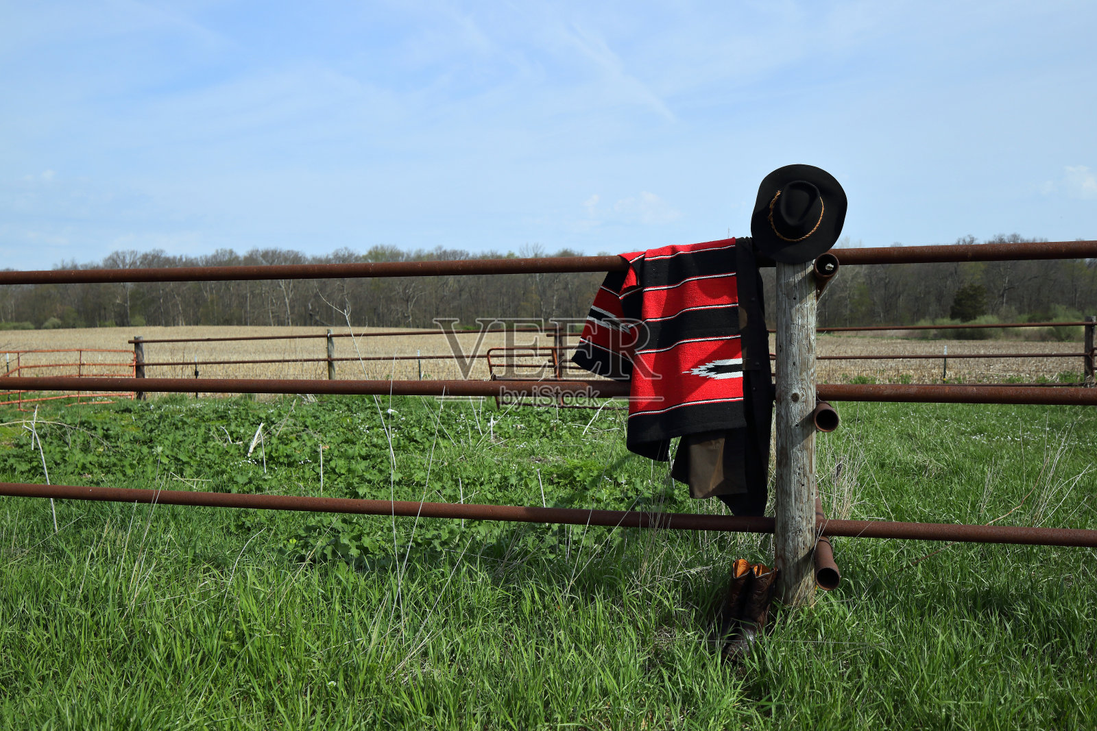 围栏上挂着牛仔的马鞍毯、靴子、帽子和抹布。照片摄影图片