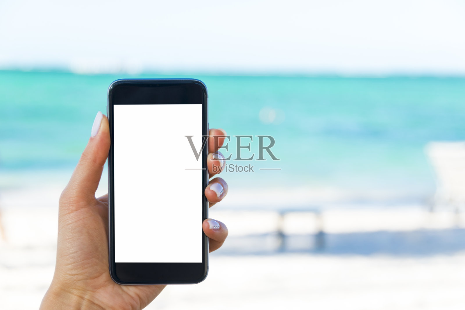 美丽女人的手在海滩上使用智能手机。智能手机白色的屏幕。屏幕空白的空照片摄影图片