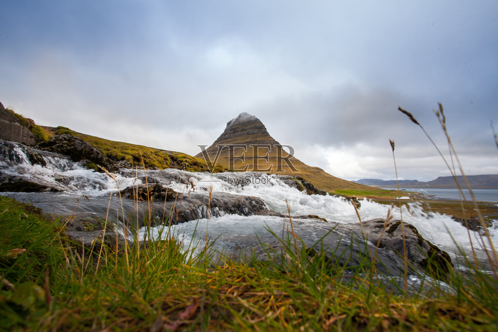 冰岛的冷水。落基山脉中的瀑布。新鲜和绿色的草。美丽的山脉在后面。照片摄影图片