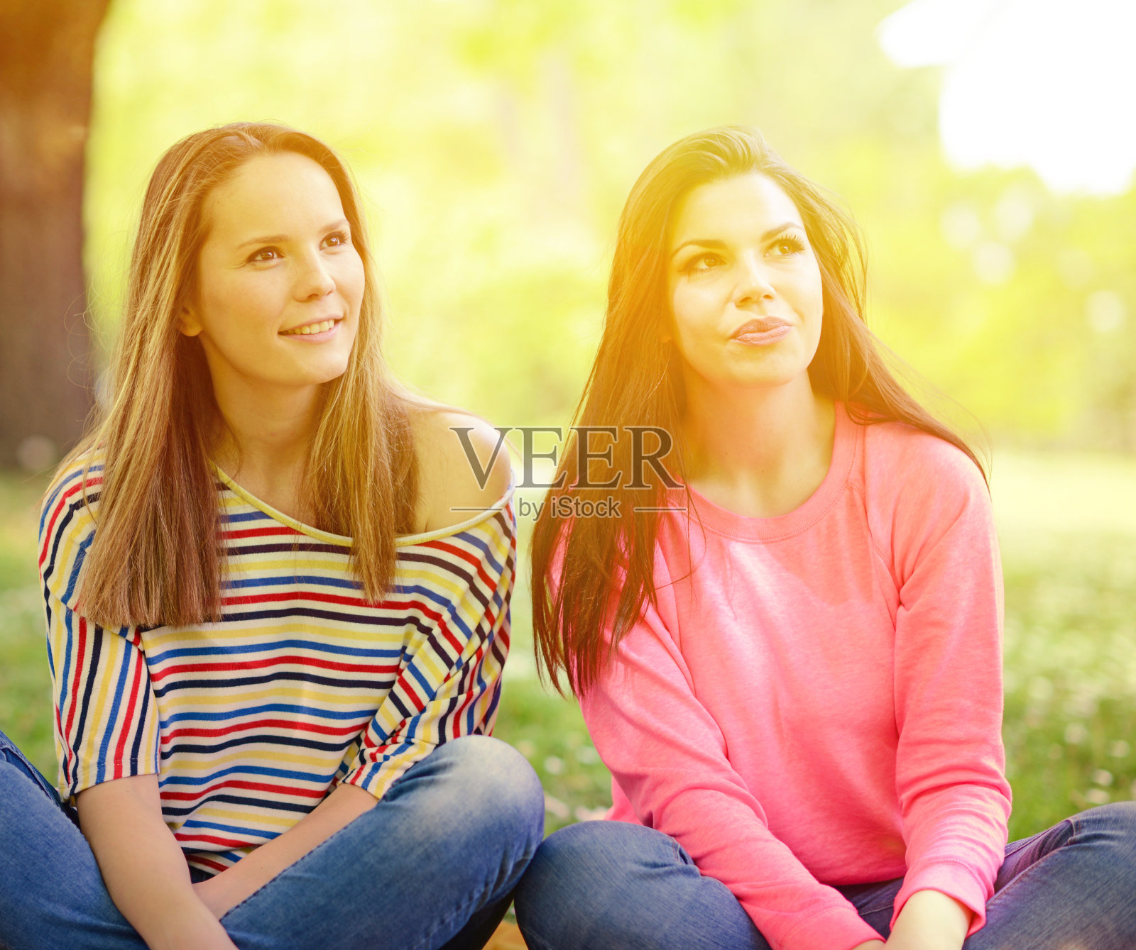 两个年轻的女孩朋友坐在草地上在夏天的一天照片摄影图片