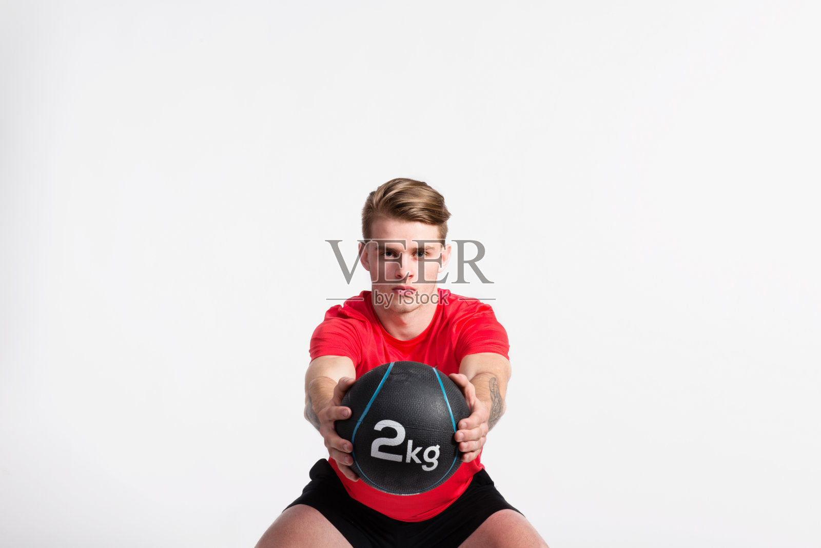 健身的人拿着实心球，做着下蹲，在摄影室里拍照。照片摄影图片