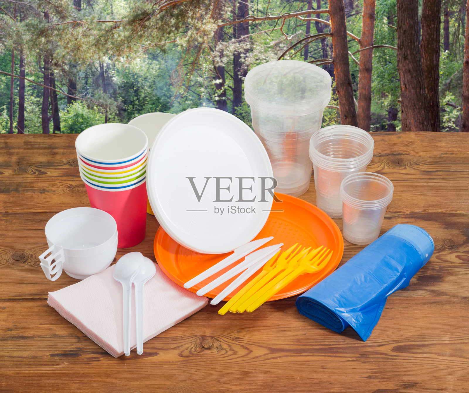 不同的一次性餐具放在木板上，背靠松林照片摄影图片