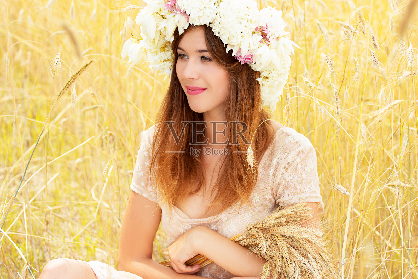 自然美景。这是一幅迷人的年轻女子的肖像，她头上戴着花，手里拿着麦子，坐在黄色的麦田里。照片摄影图片