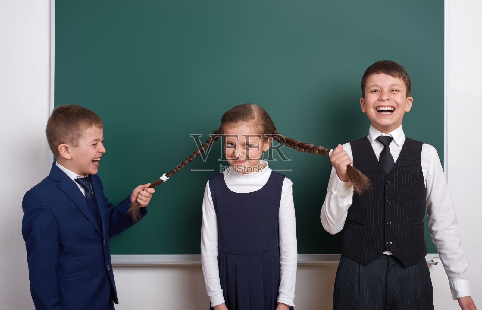 男生拉女生辫子，小学男生靠近空白黑板背景，穿着经典黑色套装，分组小学生，教育理念照片摄影图片