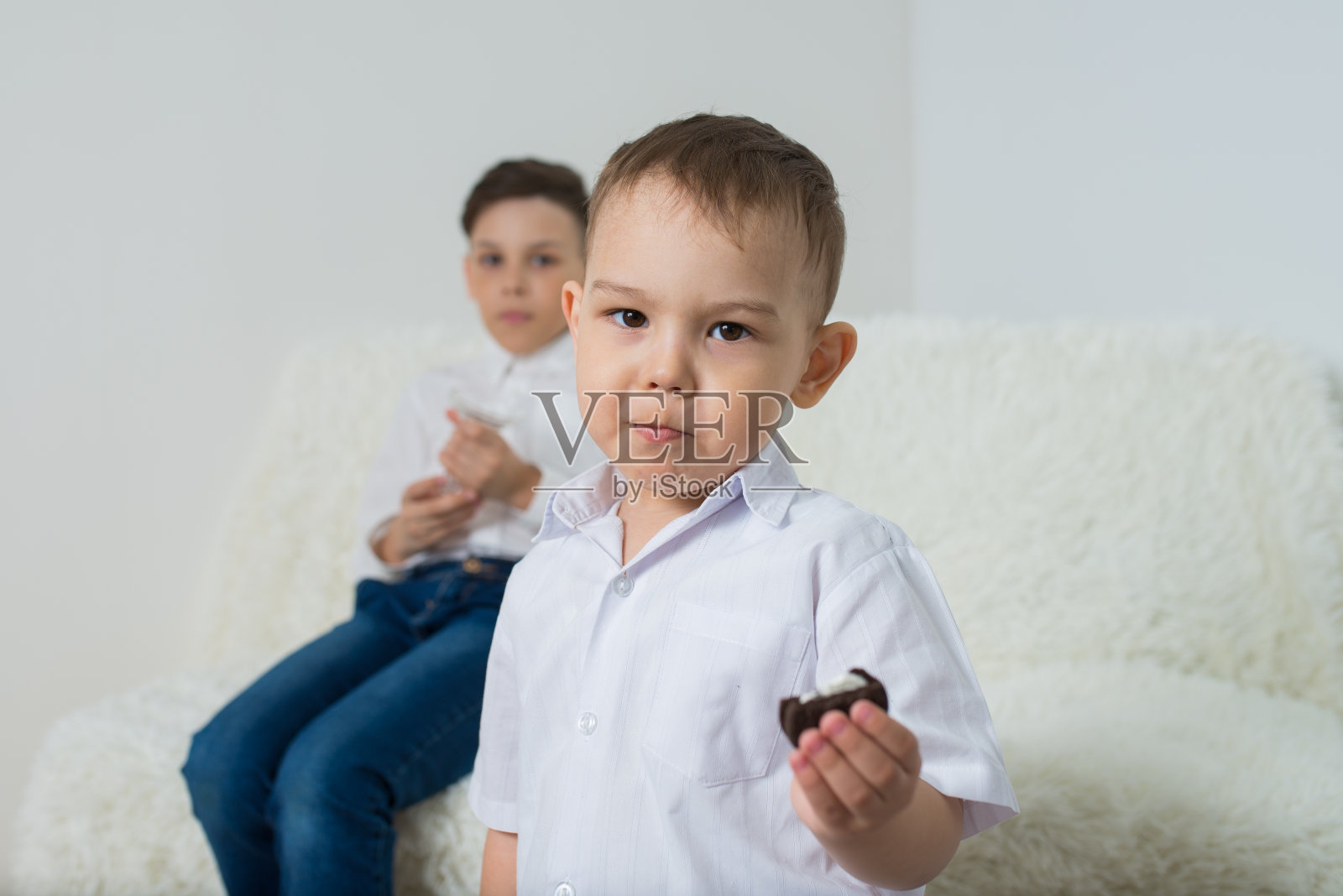 可爱认真的男孩在室内吃饼干，他的哥哥坐在后面照片摄影图片