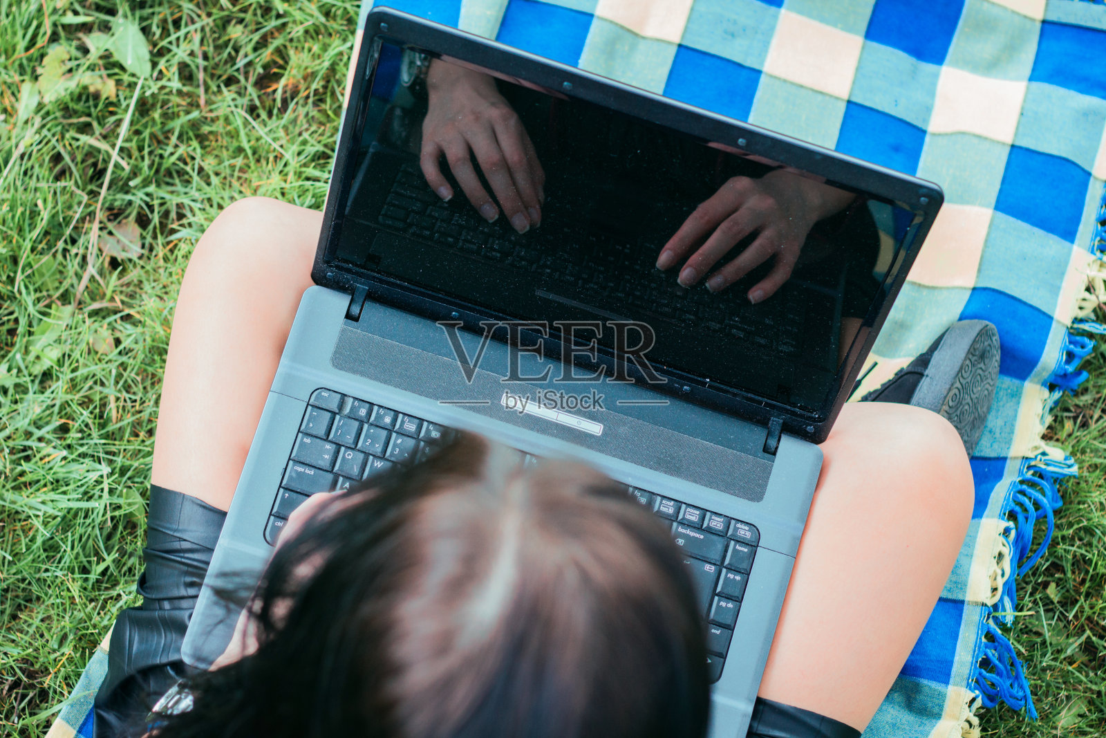 女人在公园里用手提电脑打字。反映在屏幕上。照片摄影图片