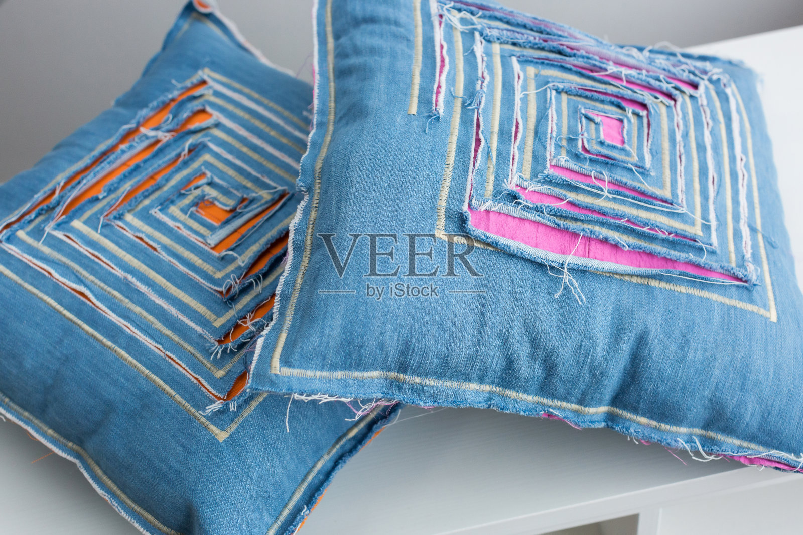 纺织品上的两个蓝色枕头在白色的背景上，近距离的枕头装饰着针线和设计师的装饰，在织物上通过可见的彩色衬里被切成迷宫的形式照片摄影图片