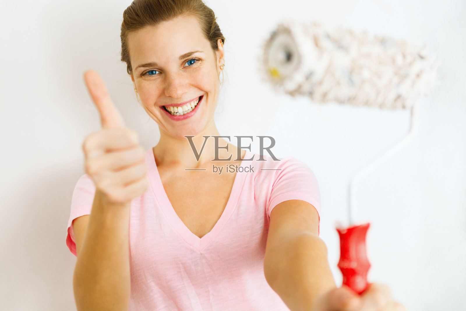 快乐的女人用滚筒刷竖起拇指。照片摄影图片