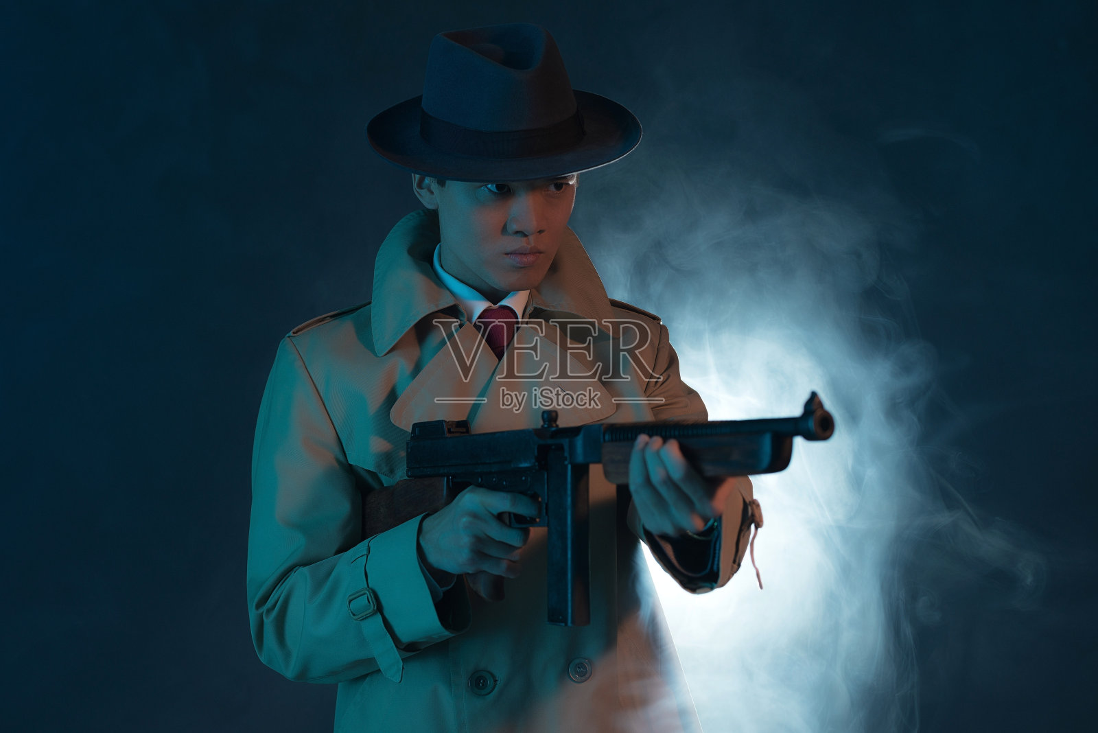 1940年穿着雨衣的亚洲黑帮时尚男士。射击的枪。照片摄影图片