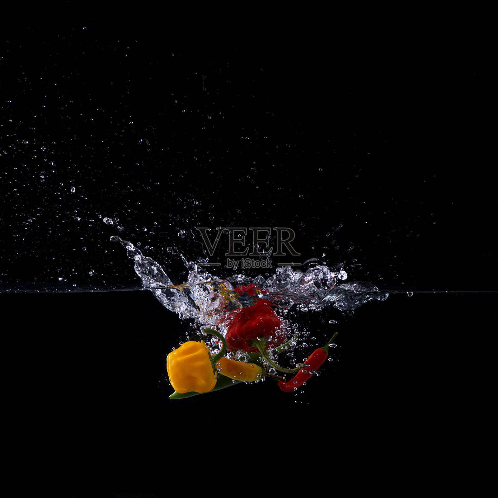 在黑色背景下，辣椒落入水中照片摄影图片