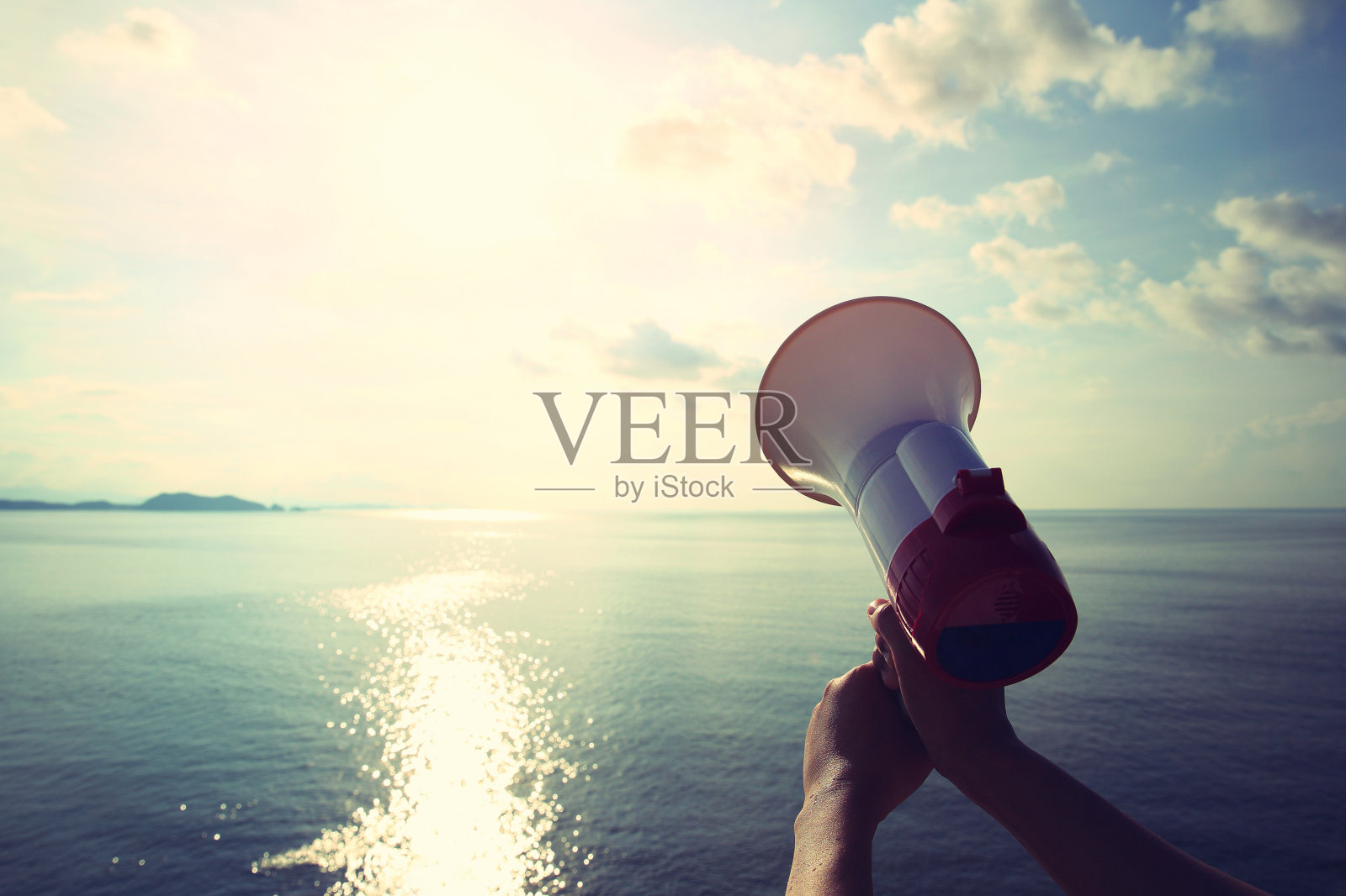 双手拿着扩音器，背景是蓝天下的海洋照片摄影图片