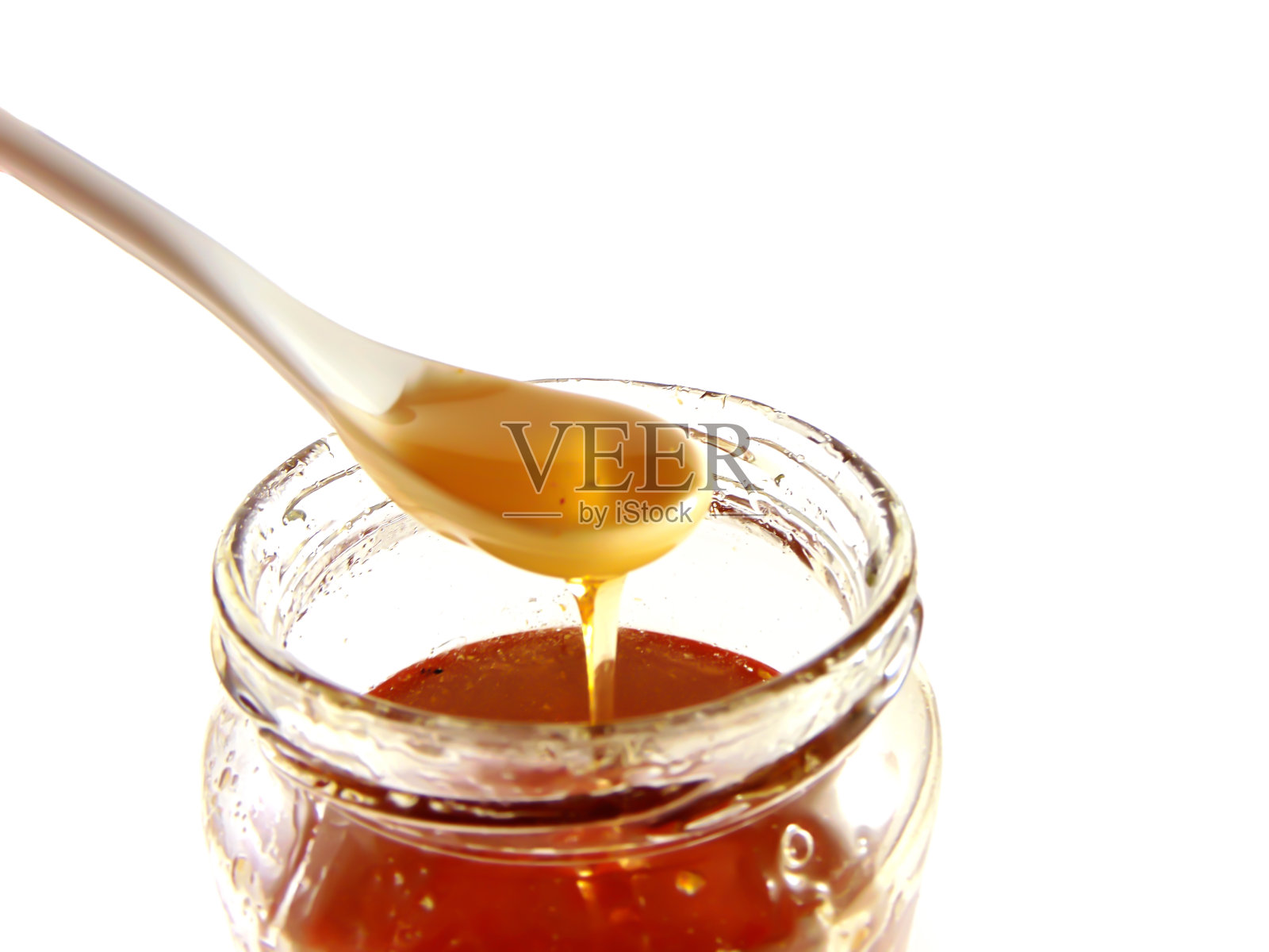 玻璃罐的蜂蜜与陶瓷勺白色的背景照片摄影图片
