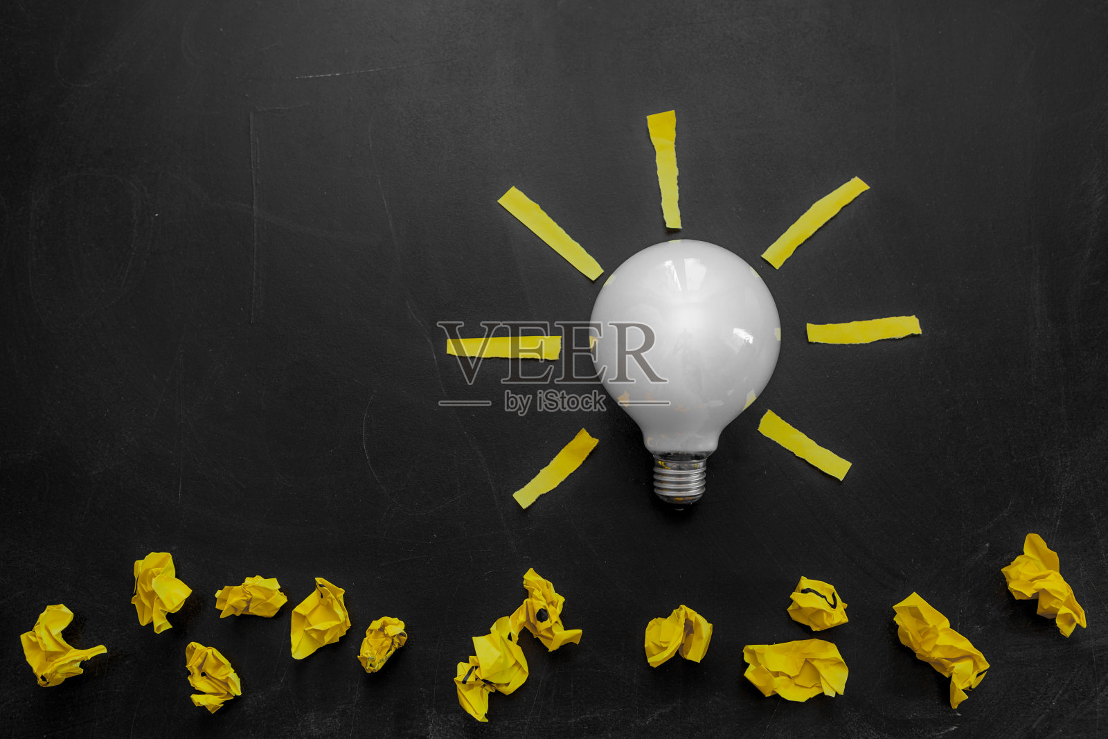 黑色黑板上的灯泡和皱巴巴的纸照片摄影图片