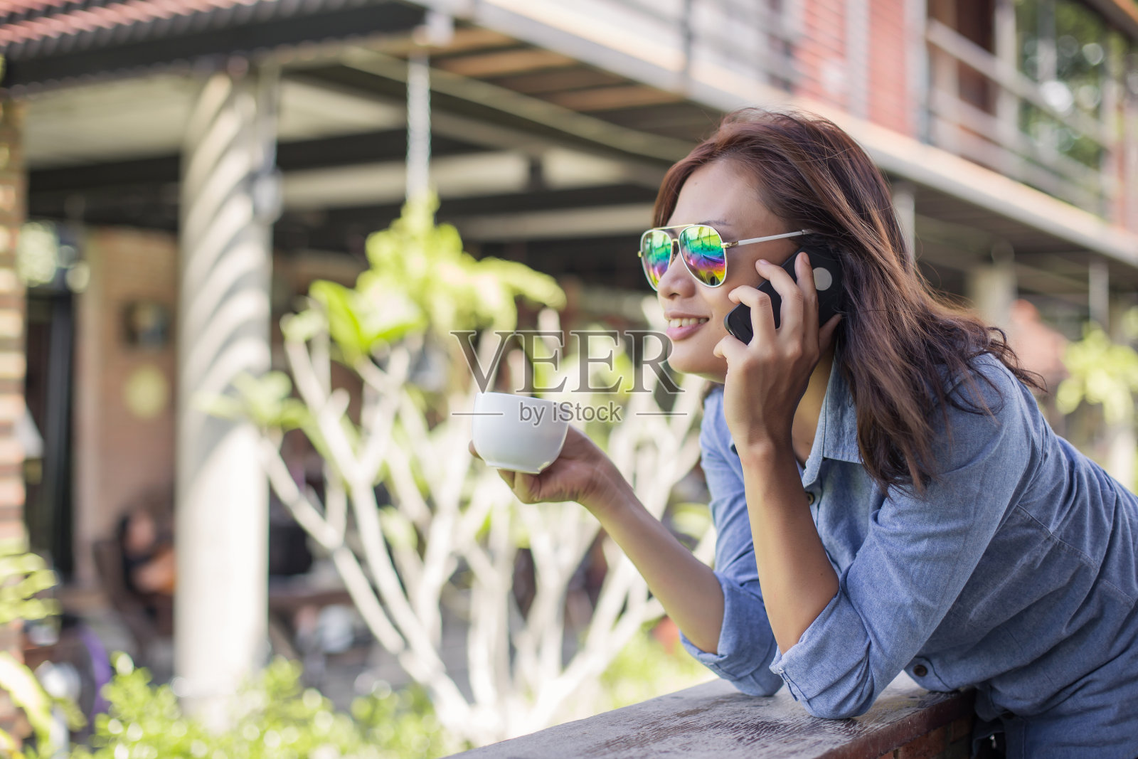 一个阳光明媚的夏天，年轻的潮女人在阳台上放松的肖像。微笑，享受大自然。照片摄影图片