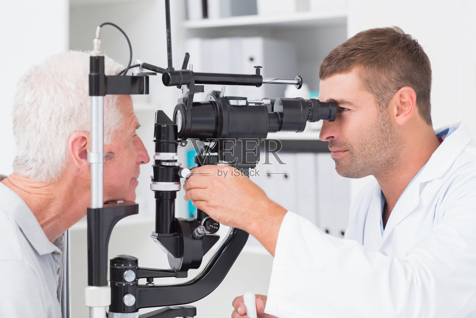 验光师通过裂隙灯检查老年患者的眼睛照片摄影图片