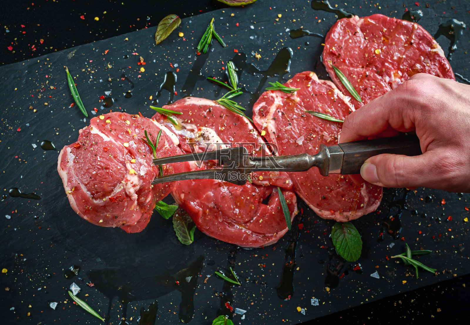 用老式叉子将生羊腿放在切菜板上，配上海盐、辣椒片、迷迭香和薄荷照片摄影图片