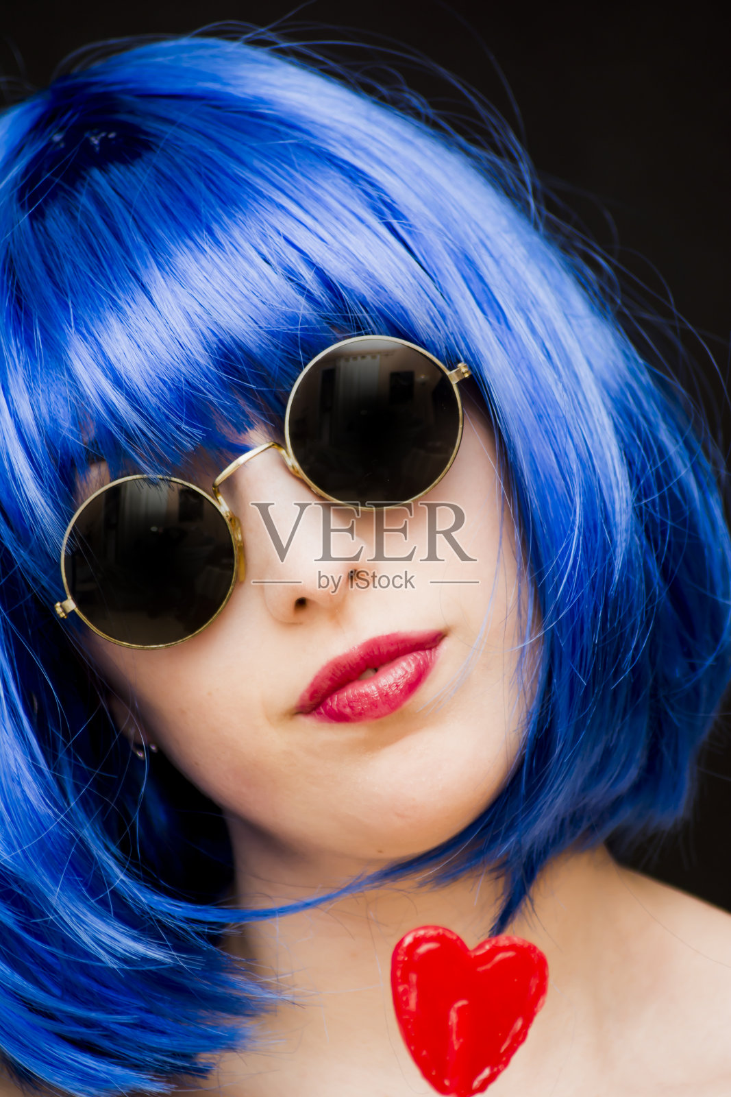 戴着蓝色假发和太阳镜的美女，手里拿着一个心形的糖果照片摄影图片