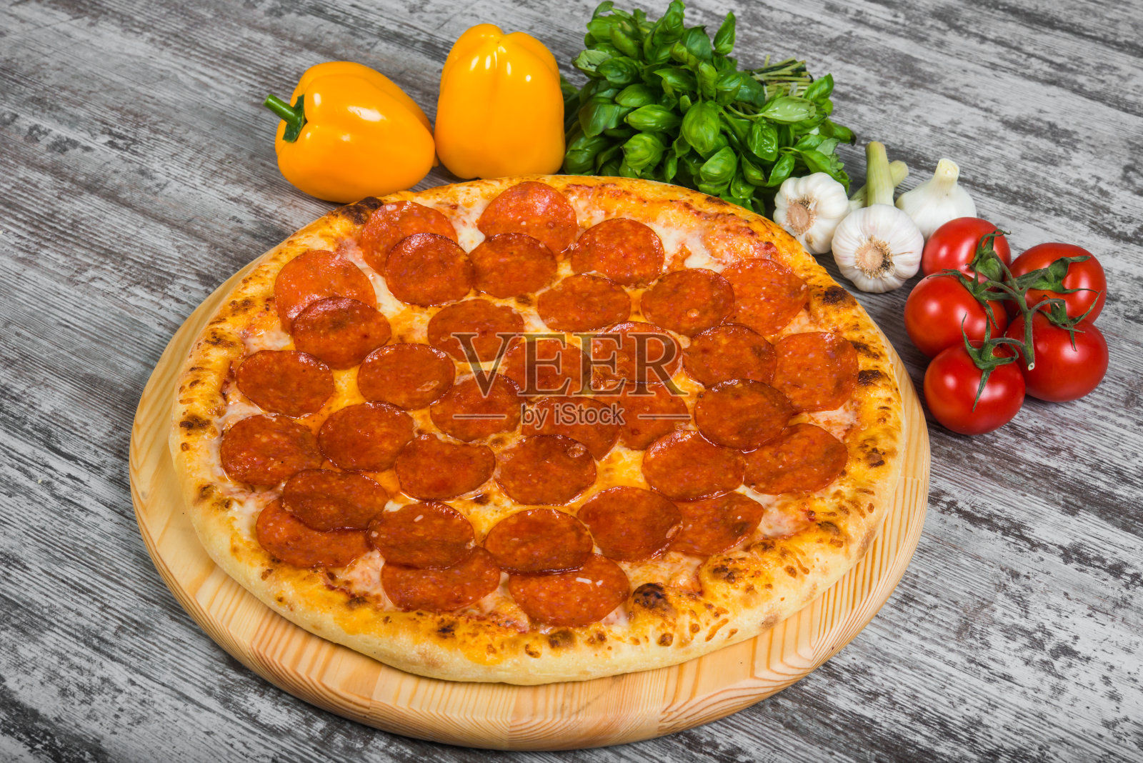 带有迷迭香和香料的意大利辣香肠披萨，以木色为背景。以绿色罗勒和新鲜蔬菜为背景的意大利披萨照片摄影图片