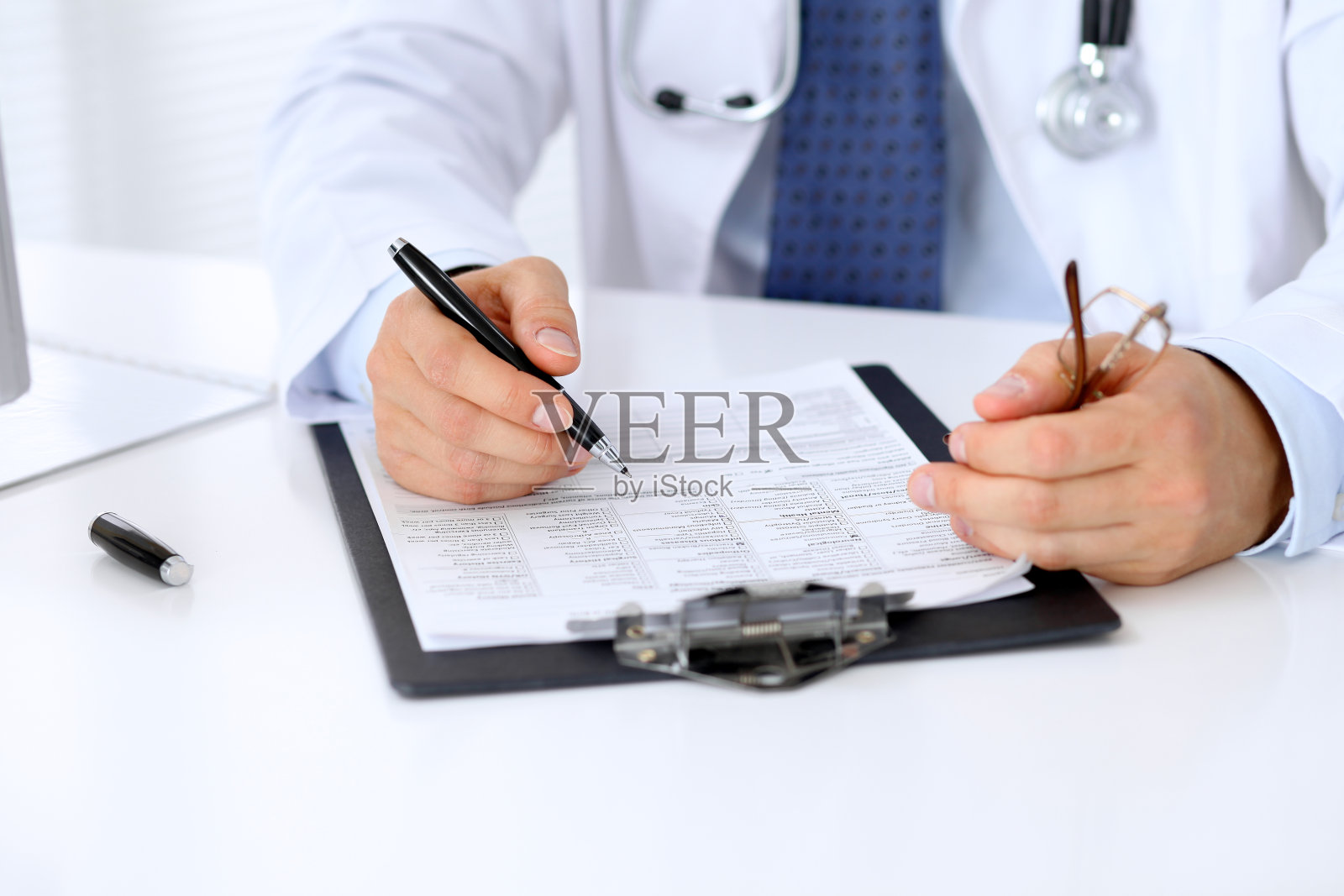 男医生正坐在桌子旁填写病史表照片摄影图片