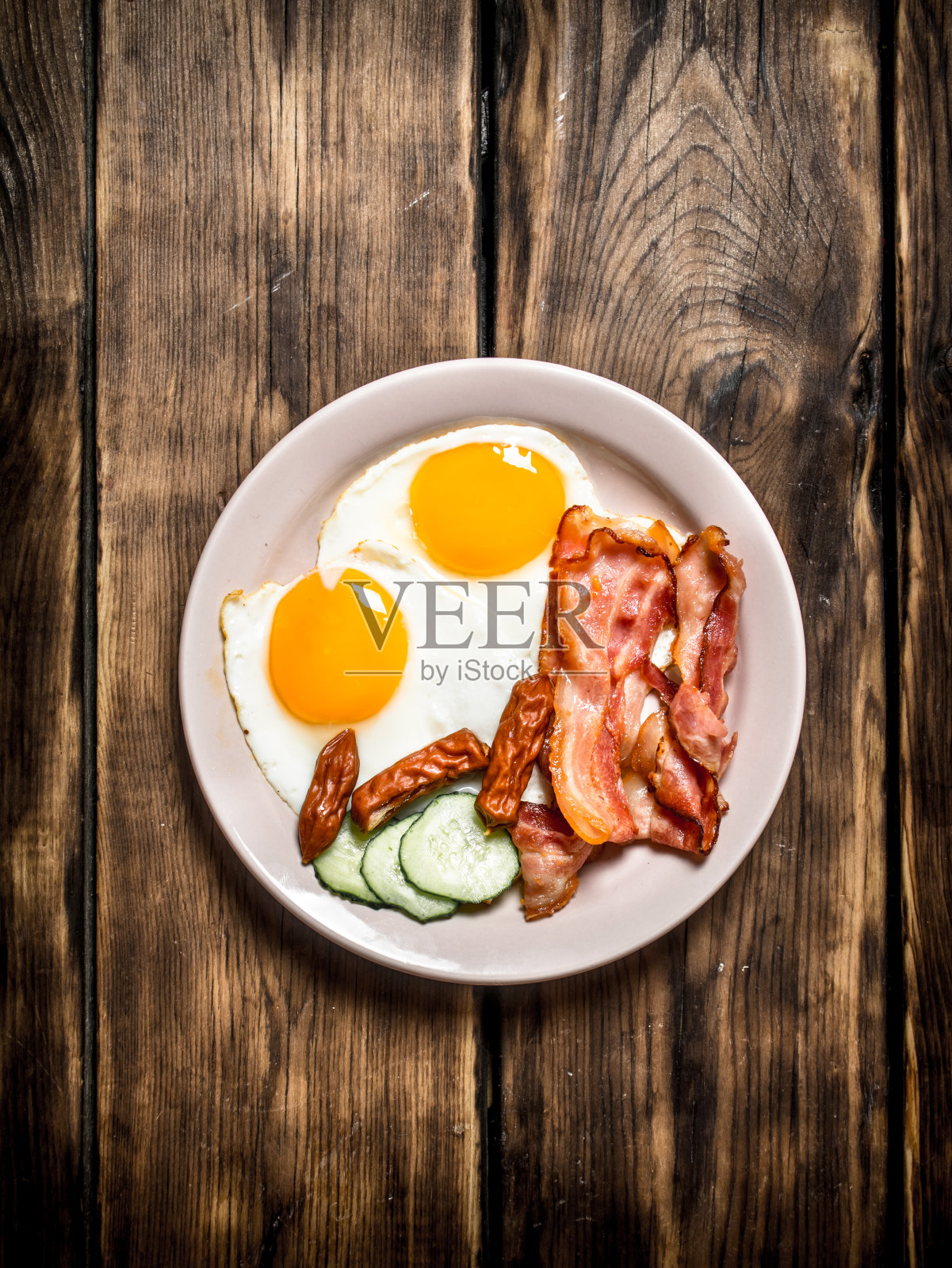 一盘煎蛋、熏肉、黄瓜和熏香肠。照片摄影图片