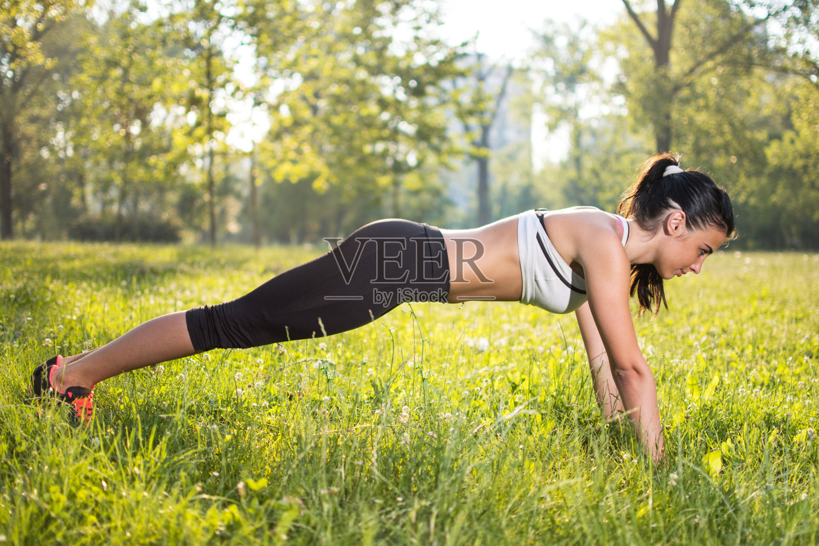 年轻的女运动员在公园里做俯卧撑。照片摄影图片
