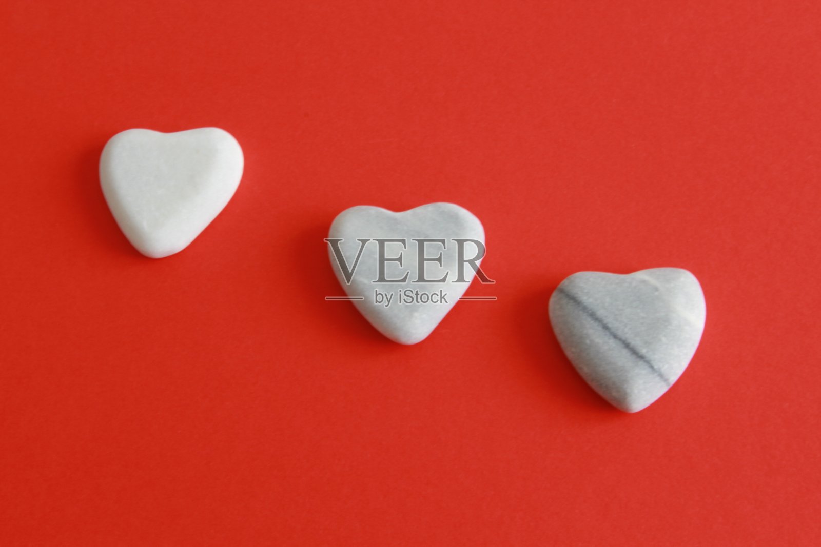 三颗石头心在红色的背景上照片摄影图片