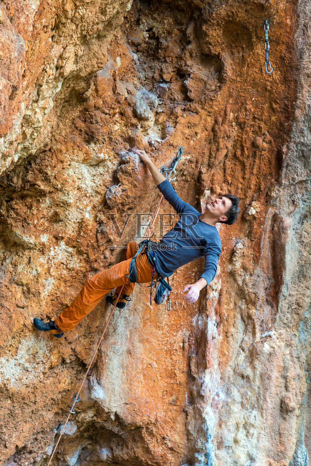 英俊的攀登者一只手挂在橙色的岩壁上照片摄影图片
