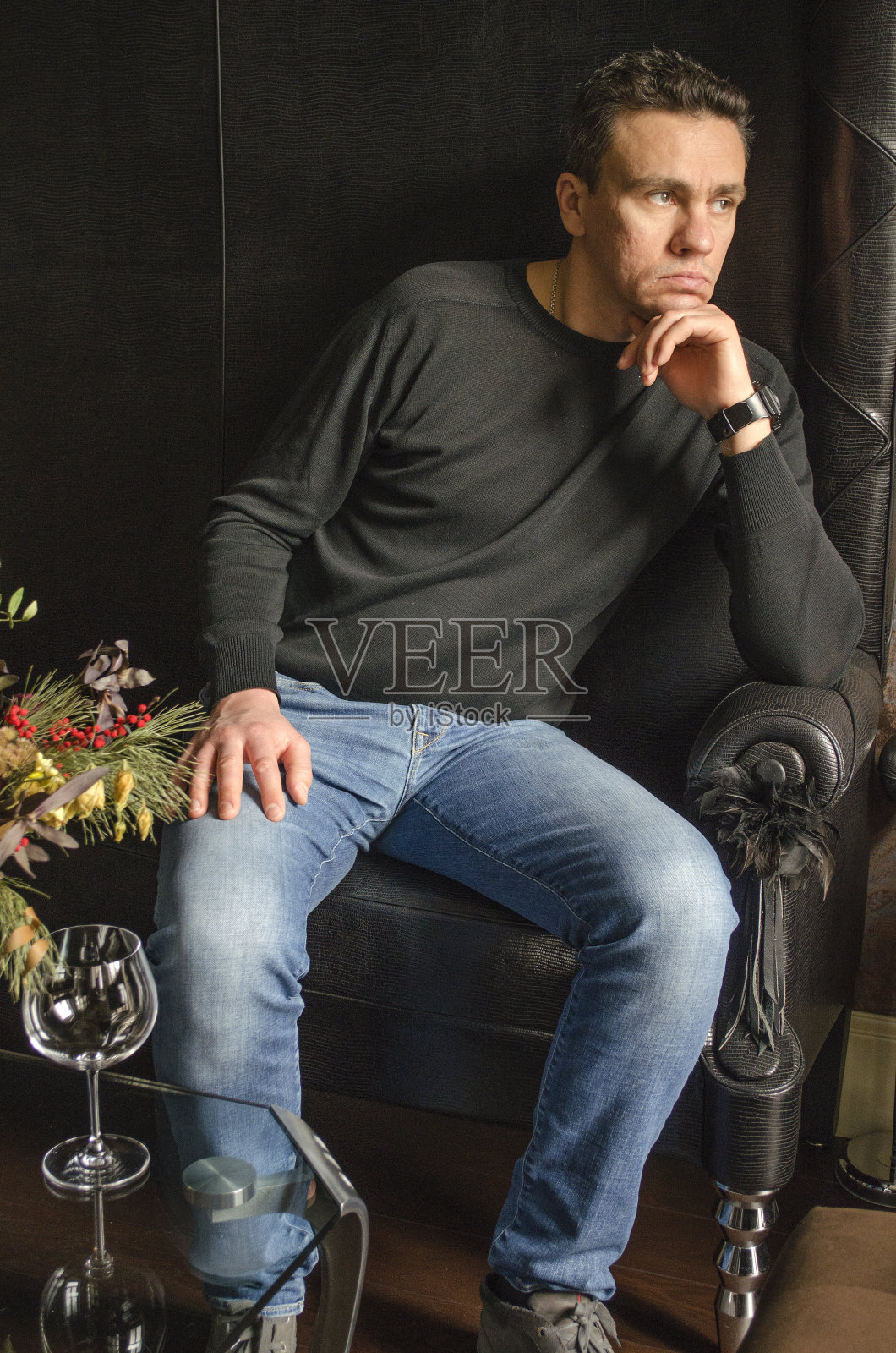 穿着黑色毛衣和蓝色牛仔裤的坐着的男人照片摄影图片