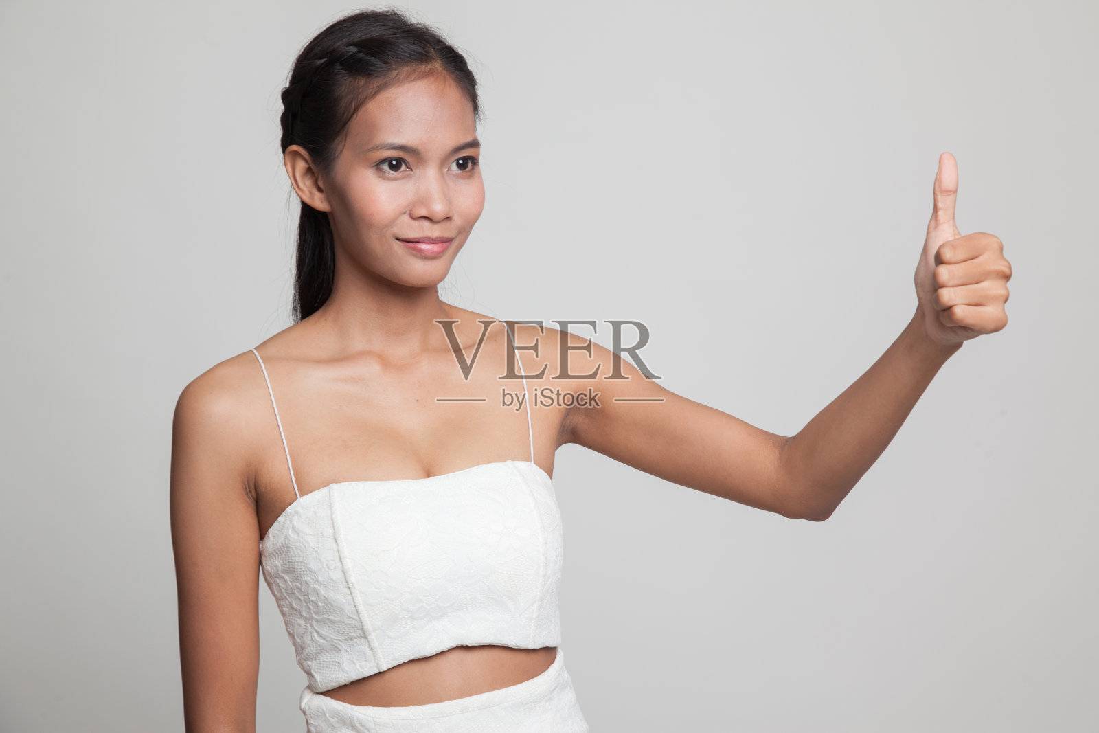 亚洲女人竖起大拇指，微笑着。照片摄影图片