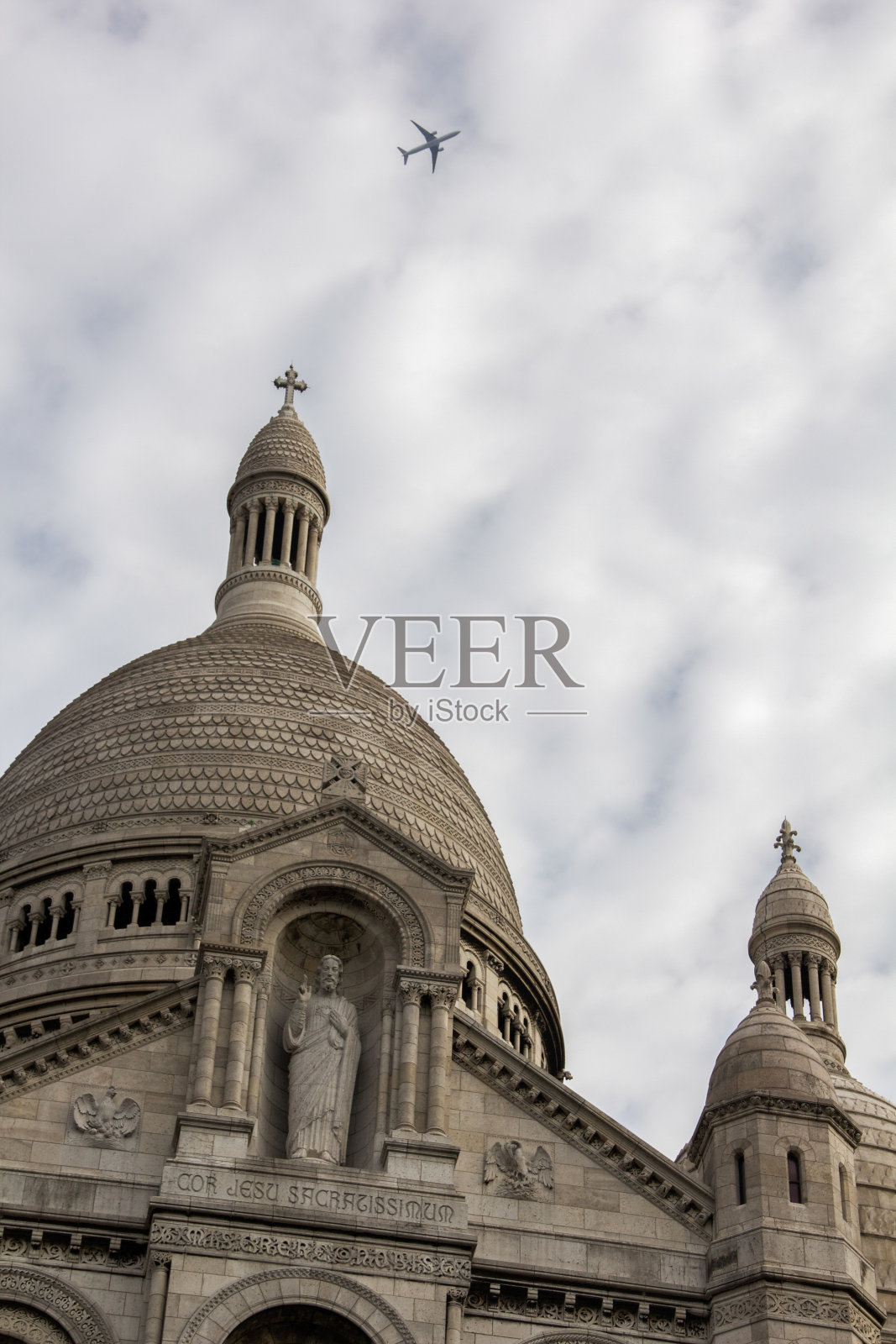 飞机在白色的天空下飞过圣心大教堂，巴黎，法国。照片摄影图片