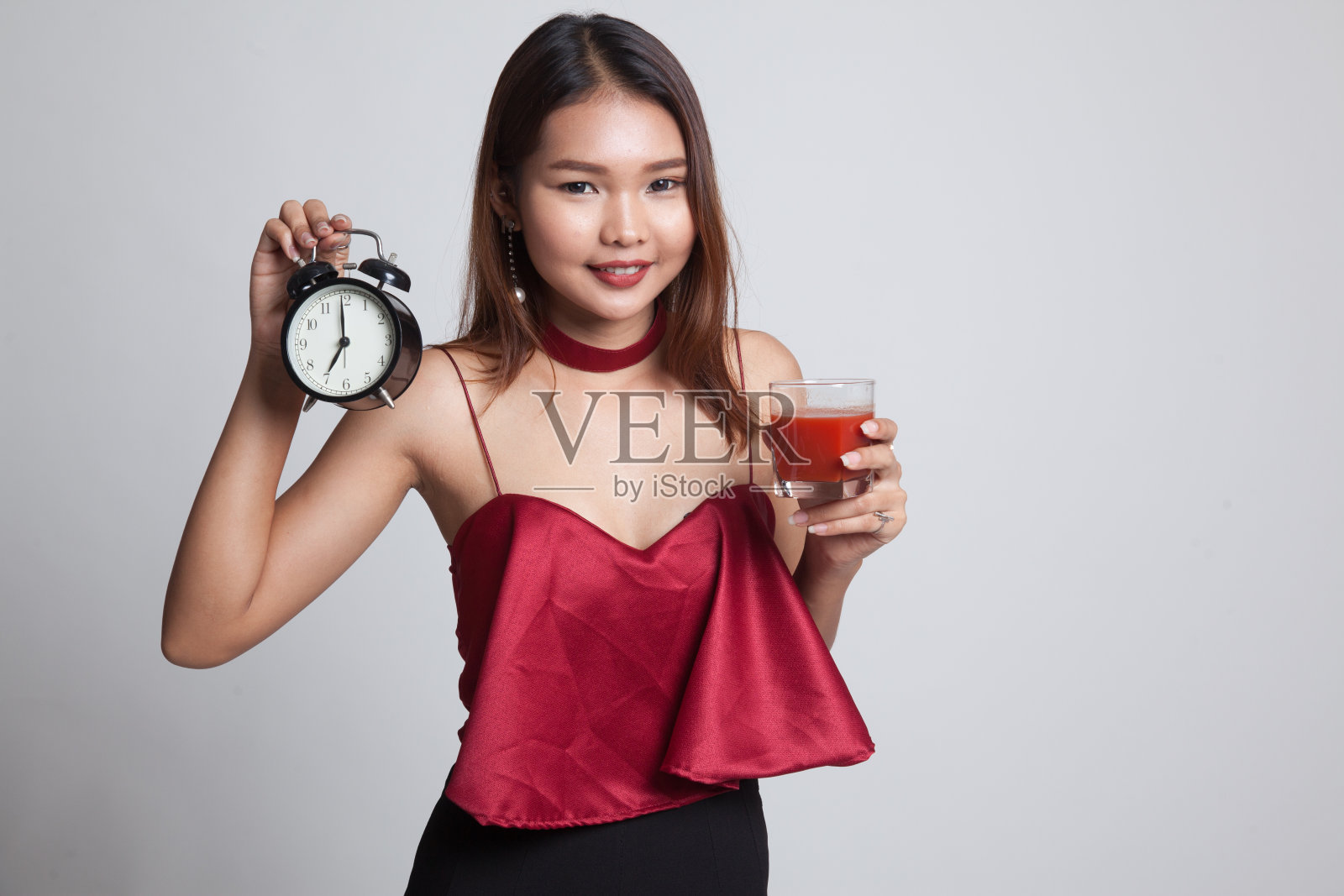 年轻的亚洲女人，喝着番茄汁和时钟。照片摄影图片