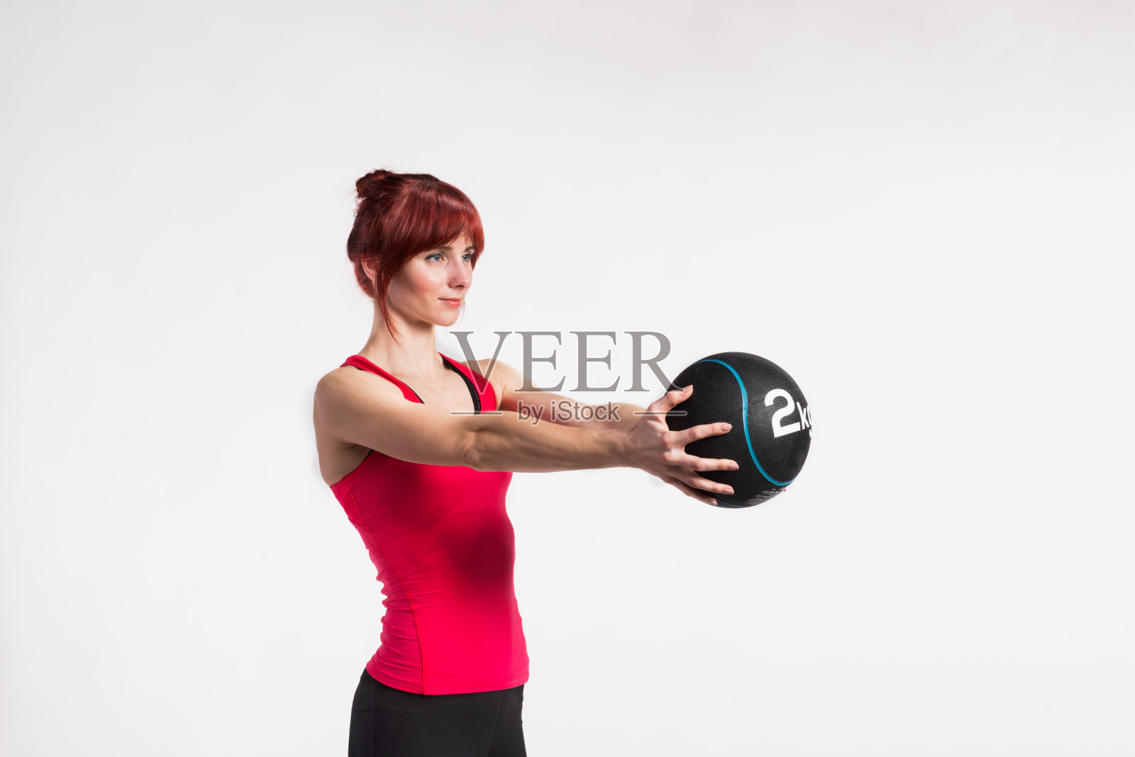穿红色背心手拿药球的健身女人。工作室拍摄。照片摄影图片