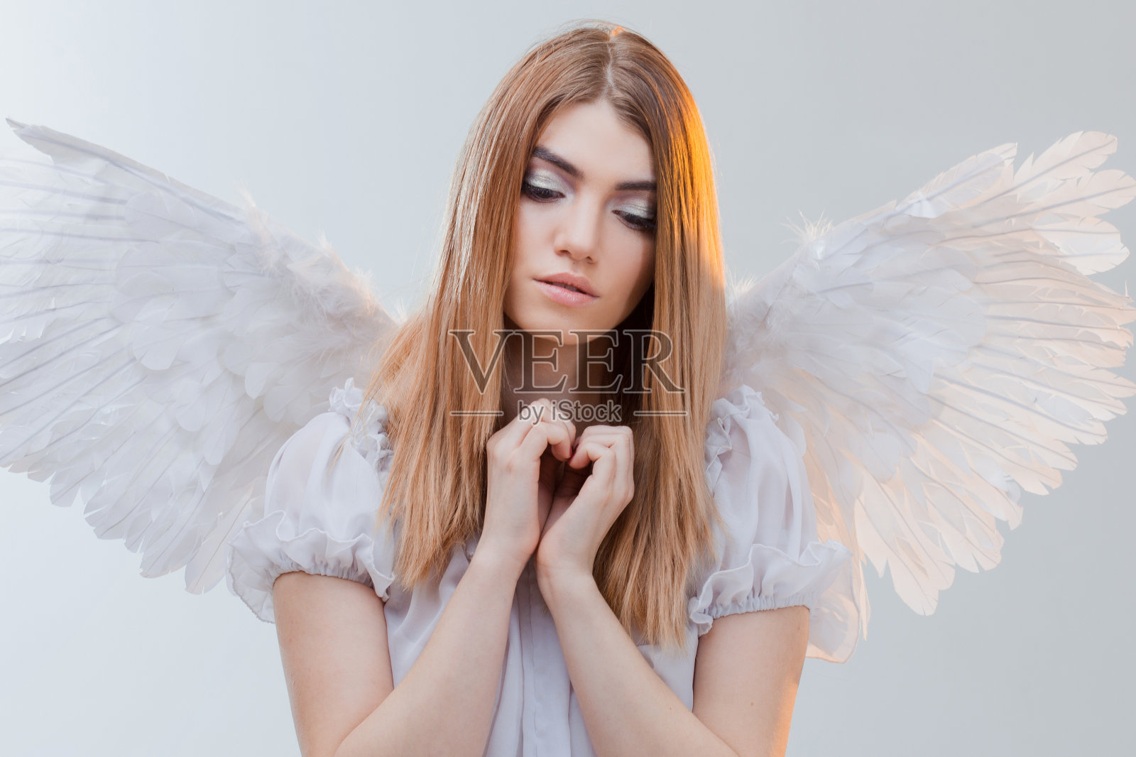 一个从天堂来的天使在手掌上拿着光。年轻漂亮的金发女孩，就像长着白色翅膀的天使。照片摄影图片