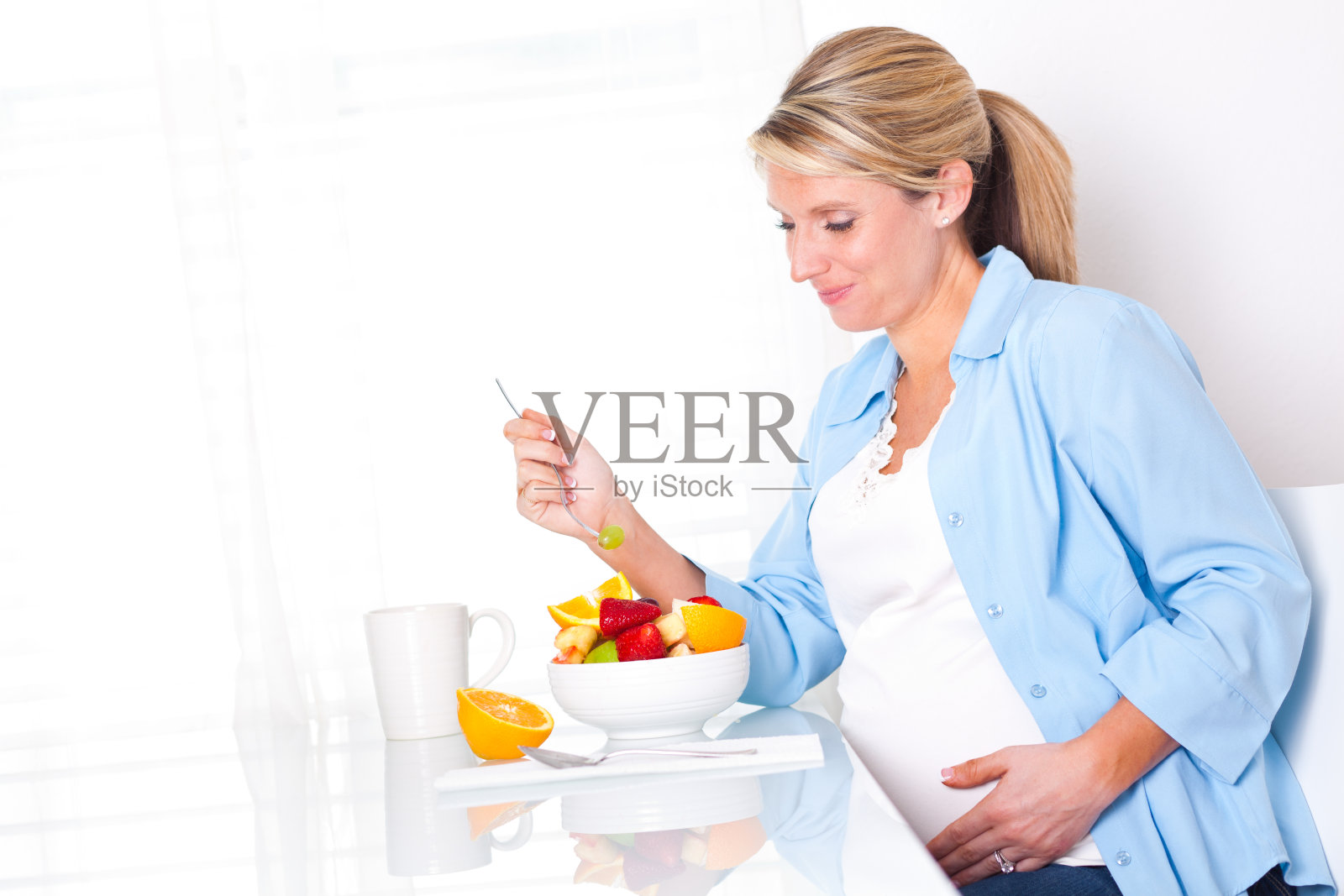 孕妇在早餐桌上吃健康水果照片摄影图片