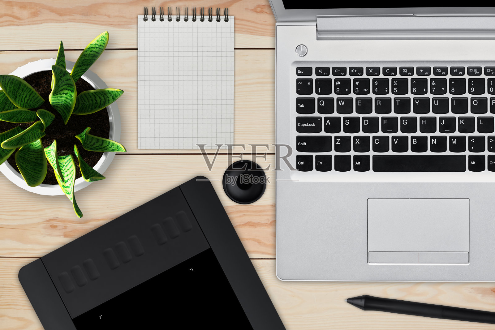 带笔记本电脑的木制书桌，带空白纸的记事本，一盆花，手写笔和用于修饰的平板电脑。专业修图师的工作空间。创意，设计，艺术和现代设备的概念照片摄影图片