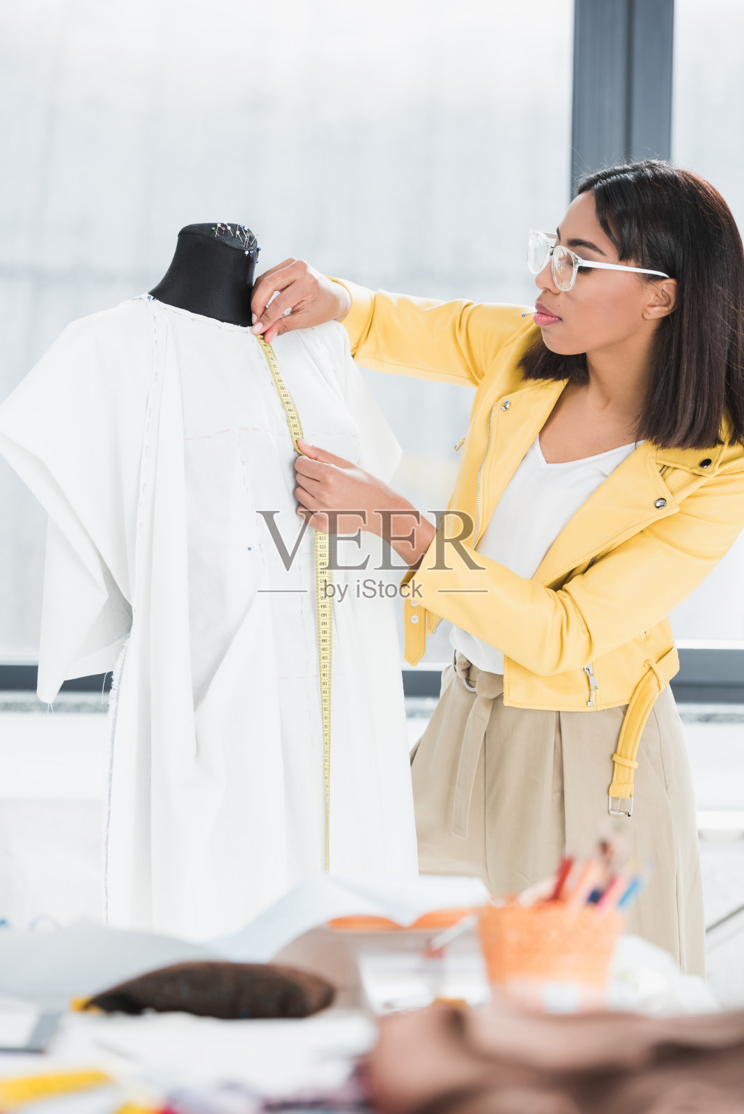 时髦的年轻女子拿着卷尺，在室内与假人一起工作照片摄影图片