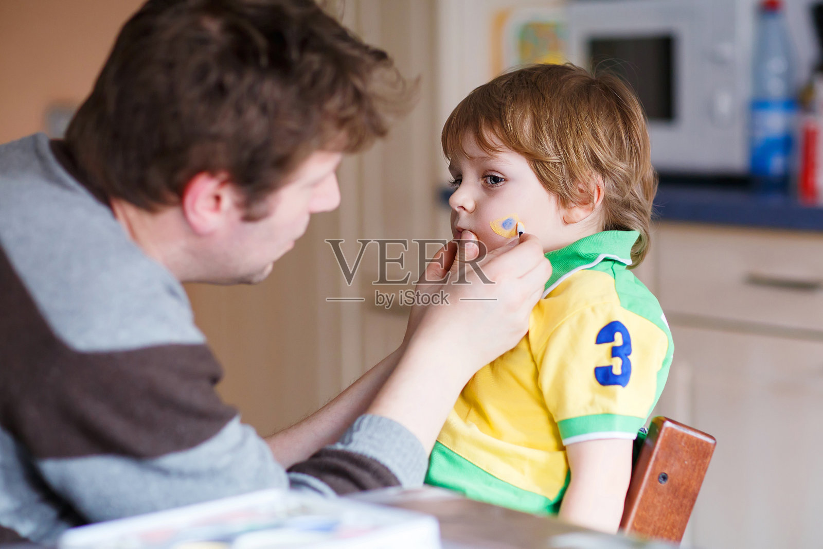 父亲在小儿子脸上画巴西国旗照片摄影图片