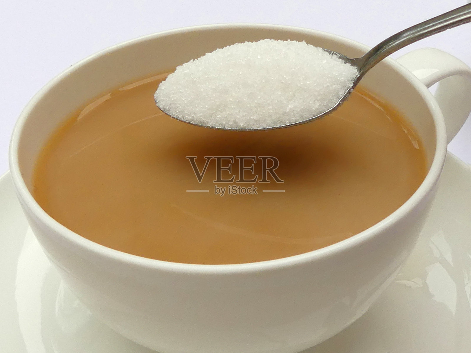 用匙舀白糖，浇在瓷杯里的茶上照片摄影图片