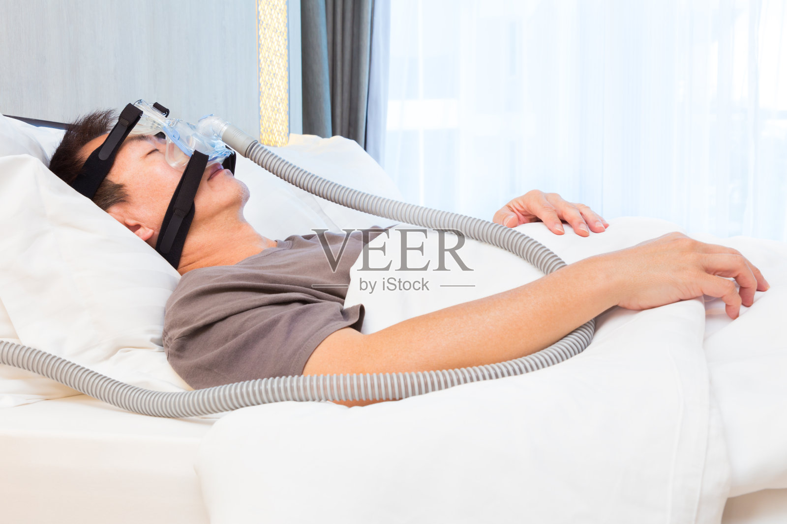 中年亚洲男子在床上睡觉，戴着连接空气软管的CPAP面罩，这是治疗睡眠呼吸暂停的设备照片摄影图片