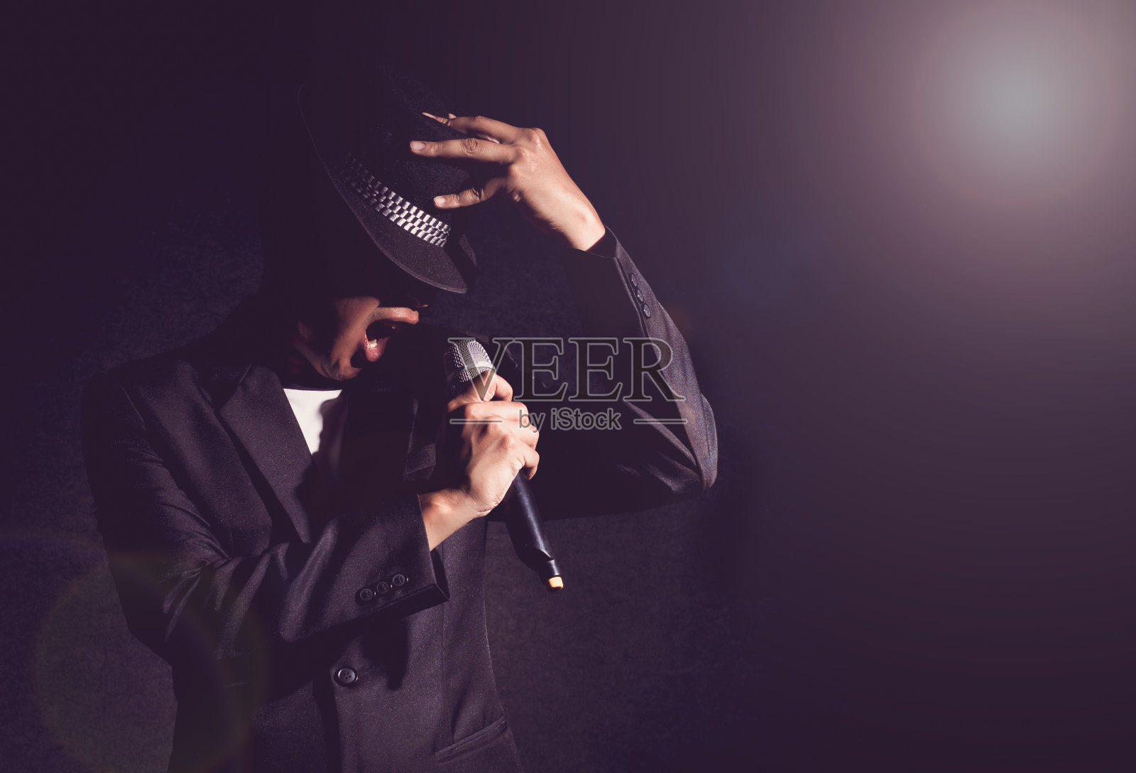 松儿手拿着麦克风，在黑色背景上唱歌，镜头从聚光灯中闪耀，音乐的概念照片摄影图片