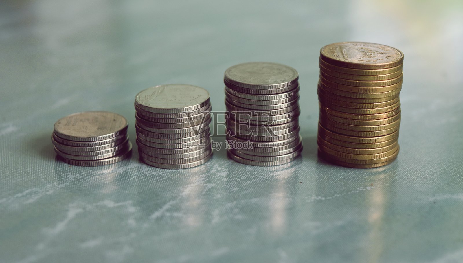 四堆硬币排在绿色大理石板上，将银和金的硬币放在图条中照片摄影图片