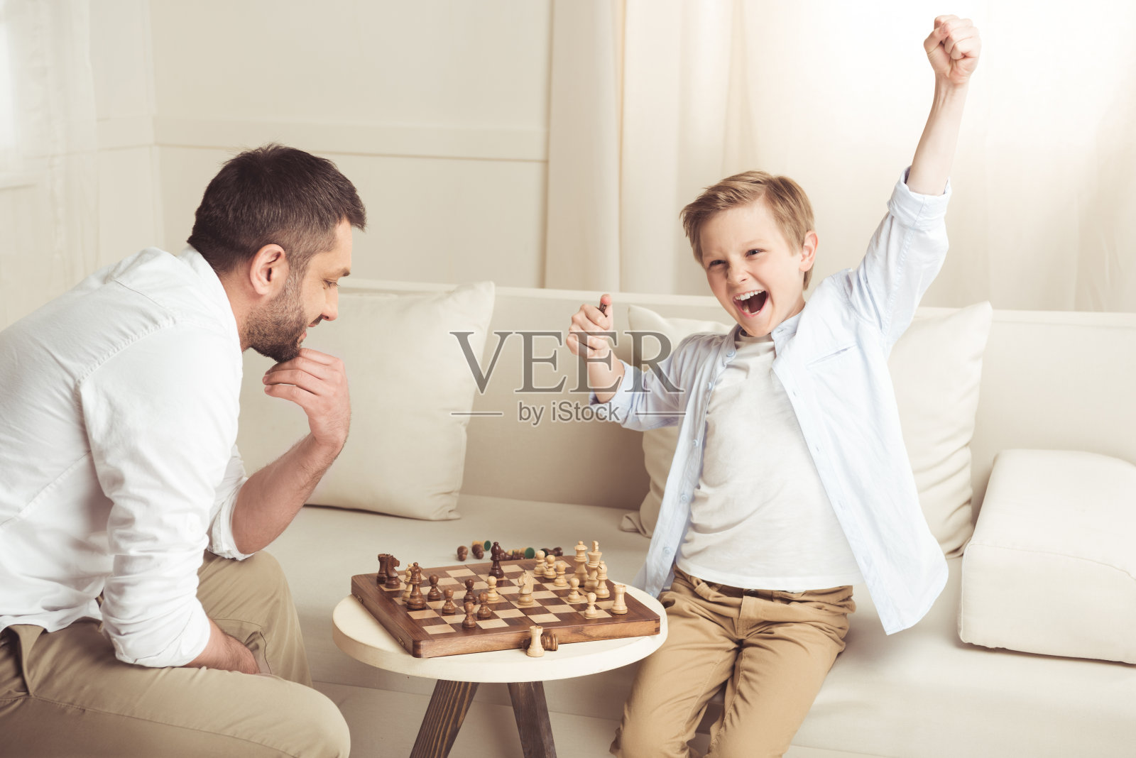 侧面的男孩庆祝成功的象棋游戏与父亲在附近照片摄影图片