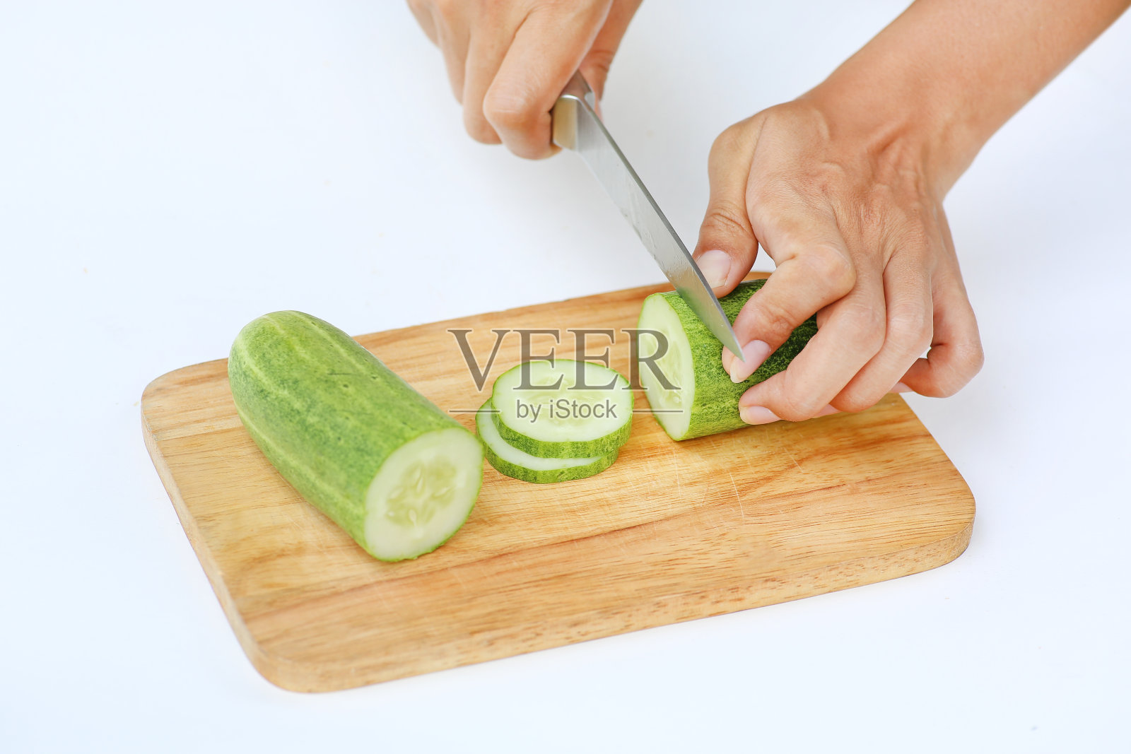 黄瓜片在木块上与刀在白色的背景。照片摄影图片