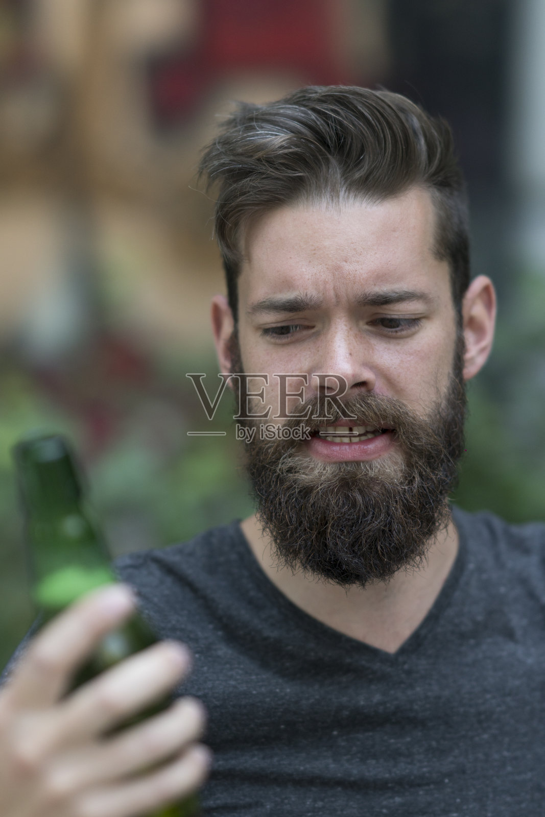 手里拿着一瓶啤酒的帅气嬉皮士。在背景中注意他的脸照片摄影图片